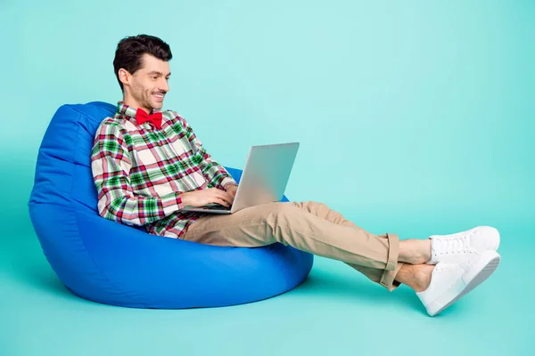Profil photo de gars assis sac tenir netbook dents sourire porter à carreaux chemise arc pantalon isolé bleu couleur arrière-plan — Photo