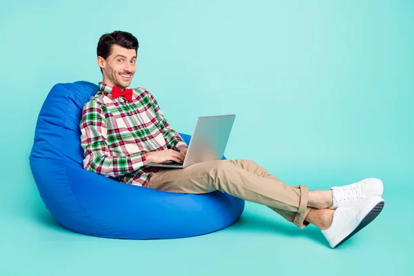 Photo of man sit bag hold pc look camera wear checkered shirt bow tie pants isolated blue color background — Stock Photo, Image