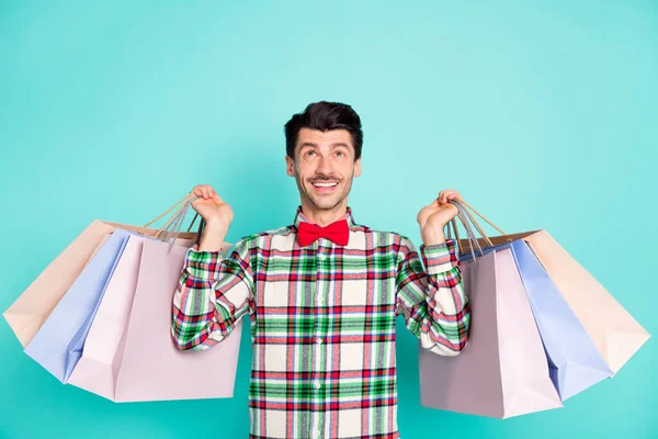 Photo of positive guy hold bags look up empty space wear checkered shirt bow isolated blue color background — Stock Photo, Image