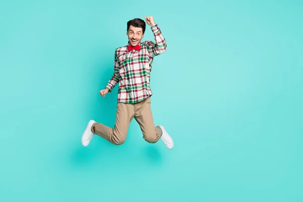 Foto de chico alegre salto levantar los puños usar camisa a cuadros moño pantalones de lazo zapatillas aisladas de color azul fondo —  Fotos de Stock