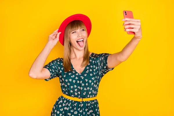 Portret van mooie gekke vrolijke meisje nemen selfie poseren aanraken hoed tonen tong plagen geïsoleerd over helder gele kleur achtergrond — Stockfoto