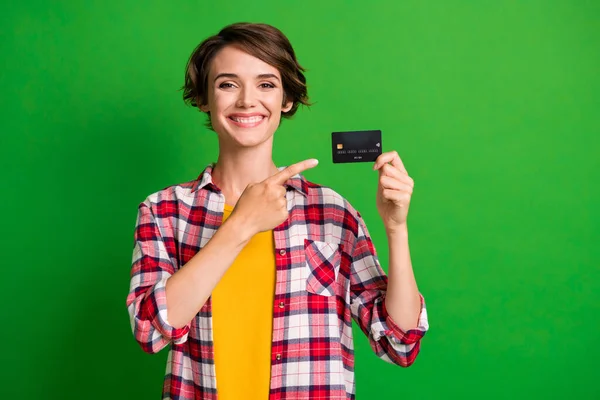 Photo of optimistic cute short hairstyle girl pointing card wear orange checkered shirt isolated over vivid green color background — Stock Photo, Image