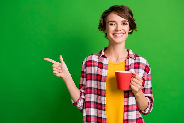Photo of funky pretty short hairstyle lady hold cup point empty space wear red shirt isolated over vivid green color background — Stock Photo, Image