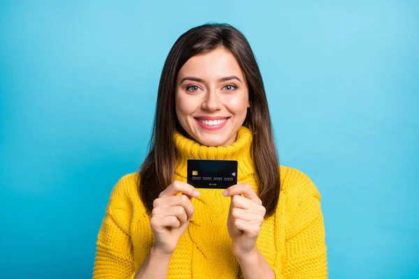 Foto de dulce encantadora joven dama usar suéter amarillo celebración de la tarjeta de crédito aislado fondo de color azul — Foto de Stock