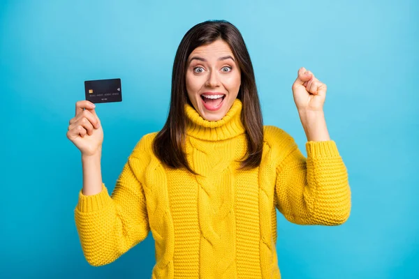 Foto van charmante gelukkige jonge dame dragen gele trui met credit card stijgende vuist geïsoleerde blauwe kleur achtergrond — Stockfoto