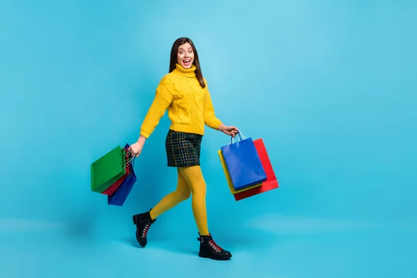 Volledige lengte foto van charmante opgewonden vrouw gekleed gele trui met winkeltassen lopen geïsoleerde blauwe kleur achtergrond — Stockfoto