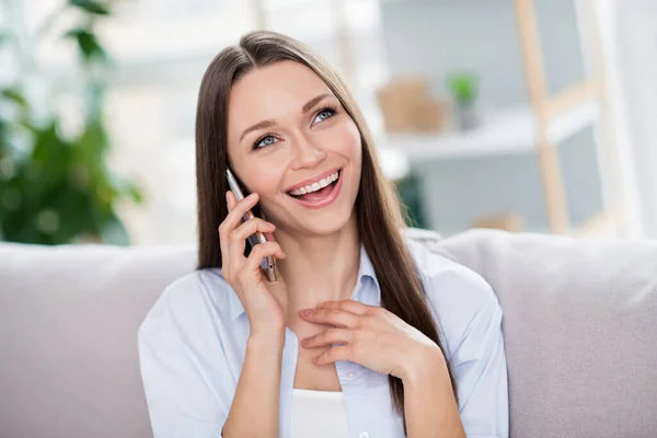 Foto van mooie optimistische brunette lang kapsel dame zitten op coach praten telefoon dragen blauw shirt alleen thuis — Stockfoto