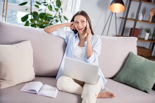 Fotografie pěkné optimistické brunetky dáma sedí s notebookem mluvit telefon vzhled psát nosit košili doma — Stock fotografie