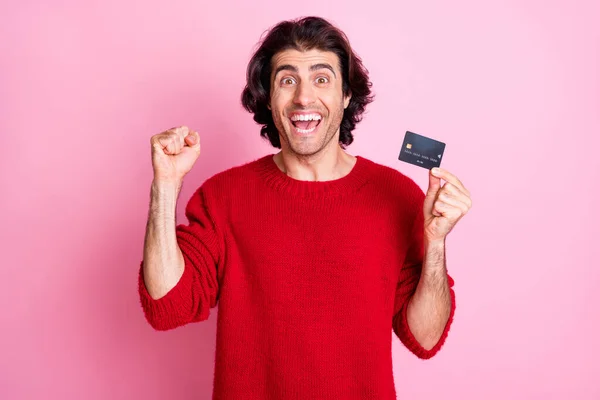 Foto portret van opgewonden vrolijke jongen vieren met vuist omhoog houden van credit card in een hand geïsoleerd op pastel roze gekleurde achtergrond — Stockfoto