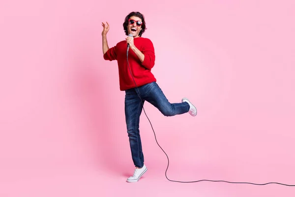 Fénykép portré férfi énekel álló egyik lábán gazdaság mikrofon a kezében visel napszemüveg elszigetelt pasztell rózsaszín színű háttér — Stock Fotó