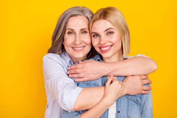 Foto retrato de la madre y la hija sonriendo abrazándose de las manos aisladas color amarillo vivo fondo — Foto de Stock