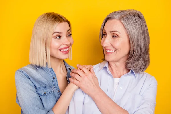 Foto retrato de la hija y la madre sonriendo cogidas de la mano mirándose el uno al otro aislado de color amarillo brillante fondo — Foto de Stock