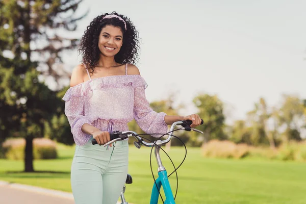 Foto de otimismo morena senhora stand com uso de bicicleta calça lilás top fora andar no parque — Fotografia de Stock