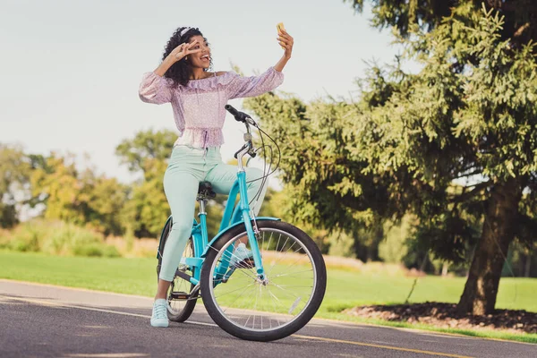 Foto de perfil de cuerpo completo de alegre hermosa mujer de piel oscura sentarse en bicicleta hacer selfie dedos muestran v-signo pasar tiempo al aire libre —  Fotos de Stock