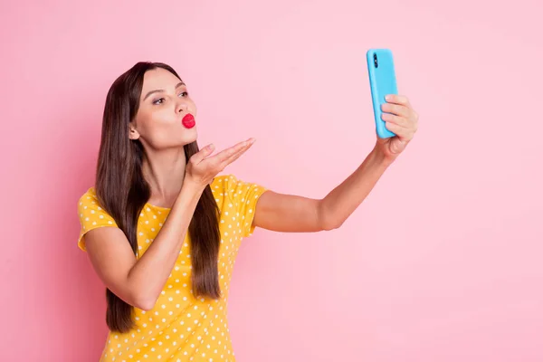 Photo of flirty young woman send air kiss hand phone take selfie wear yellow dotted t-shirt isolated on pink color background — Stock Photo, Image