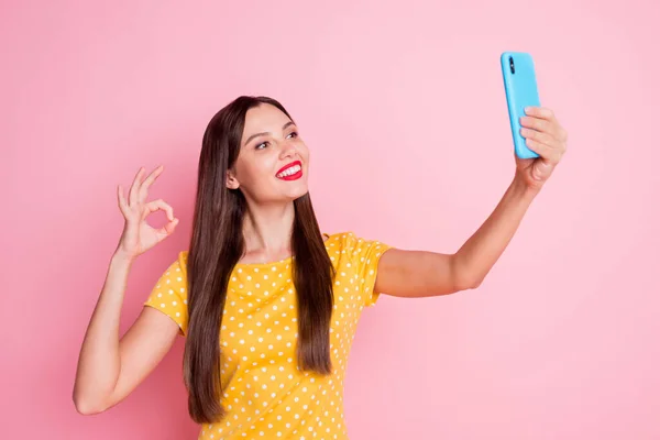 Foto de mujer morena bonita hacer signo bien hacer selfie desgaste amarillo punteado camiseta aislada sobre fondo de color rosa — Foto de Stock