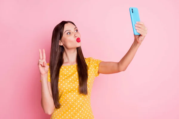 Foto de mujer joven de cabello castaño usar amarillo punteado camiseta hacer v-signo tomar selfie enviar aire beso aislado en color rosa fondo — Foto de Stock