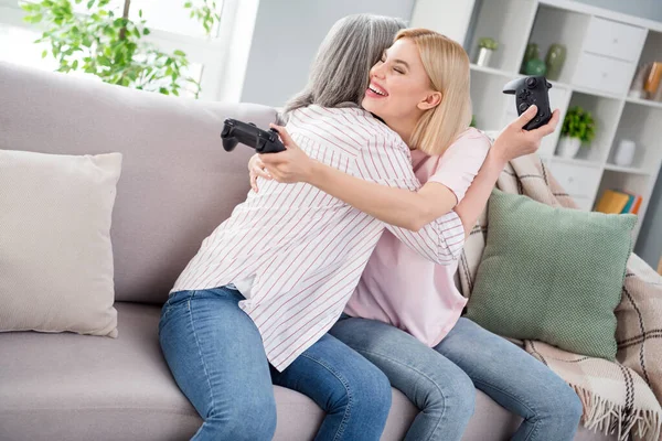 幸せな家族の母親と娘抱擁座ってソファホールドジョイスティックゲーム室内家の中 — ストック写真