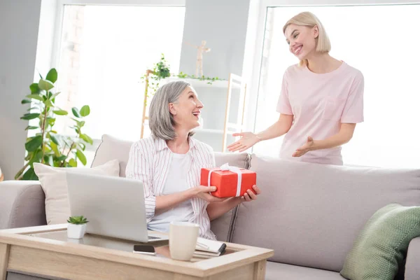 Фото щасливої сірої волохатої жінки і блондинки сидять диван отримати подарунок гарний настрій всередині будинку будинку — стокове фото