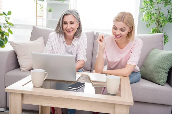 Foto de la madre rubia de pelo gris y la hija sentarse sofá uso portátil escribir nota dentro de casa casa en interiores — Foto de Stock