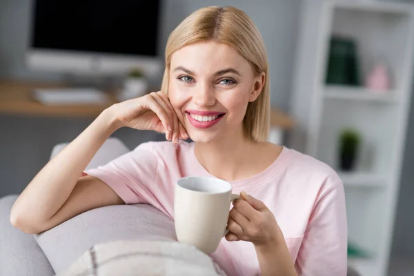 Foto van vrolijke charmante mooie jonge vrouw zitten sofa drinken koffie mok binnen huis — Stockfoto