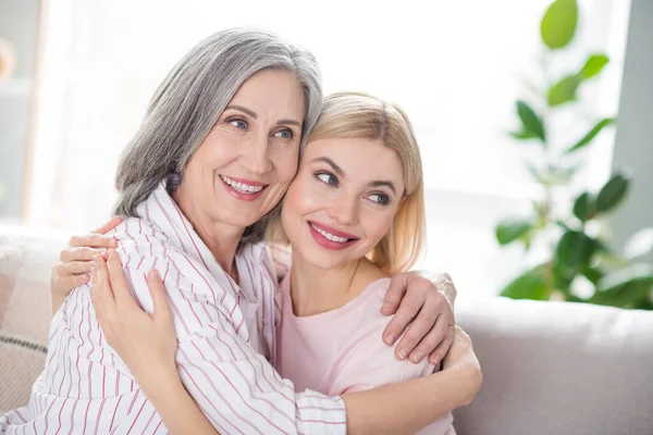 Portrait of two charming cheerful ladies sit on sofa hugging each other look far away beaming smile indoors — Stock Photo, Image