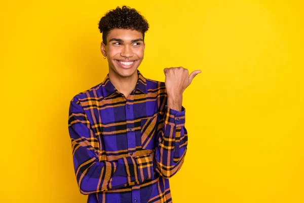 Foto retrato del joven sonriendo mostrando el pulgar mirando en el espacio en blanco aislado vibrante fondo de color amarillo —  Fotos de Stock