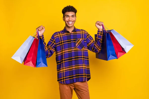 Foto de joven alegre chico negro feliz sonrisa positiva mantenga bolsas de compras viernes negro aislado sobre fondo de color amarillo —  Fotos de Stock