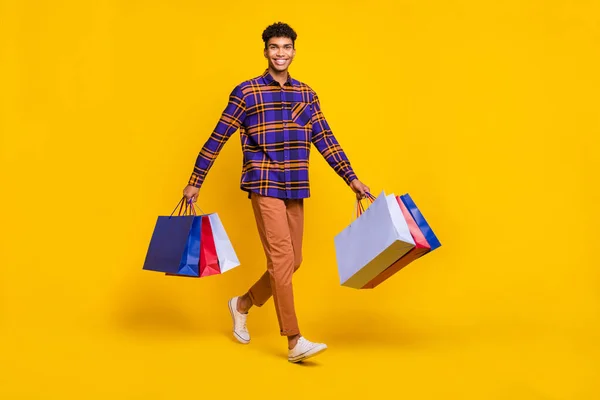 Foto de cuerpo completo de joven alegre afro hombre feliz sonrisa positiva ir caminar paso compras bolsas aisladas sobre fondo de color amarillo — Foto de Stock