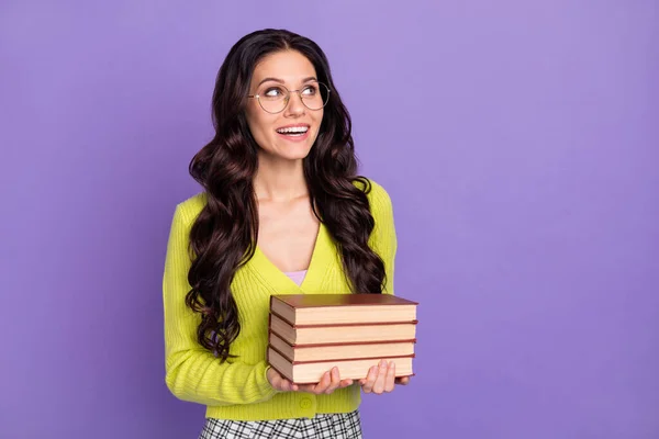 Foto de otimista agradável morena encaracolado senhora olhar espaço vazio segurar livros usar óculos camisola verde isolado no fundo roxo — Fotografia de Stock