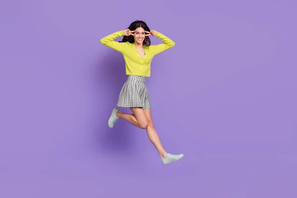 Full Size Profilfoto von optimistisch schön brünett lockige Dame springen gehen ahow V-Zeichen tragen Pullover Rock Turnschuhe isoliert auf lila Hintergrund — Stockfoto