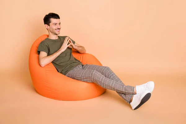 Photo of guy sit beanbag hold fingers look empty space wear green t-shirt pants footwear isolated beige color background — 图库照片