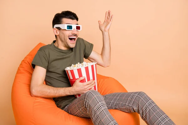 Full size foto van jonge gelukkig opgewonden man in 3D bril zitten stoel eten popcorn horloge bioscoop geïsoleerd op beige kleur achtergrond — Stockfoto