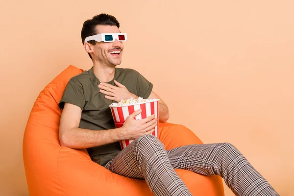 Photo portrait of man in chair watching comedy film eating pop corn laughing isolated on pastel beige color background