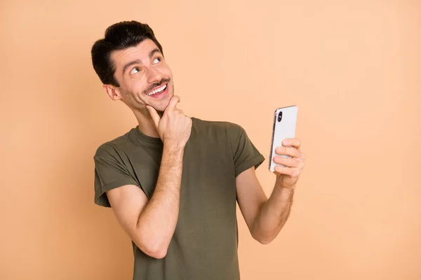 Photo portrait of man browsing internet with smartphone looking blank space dreaming thoughtful isolated on pastel beige color background — 图库照片