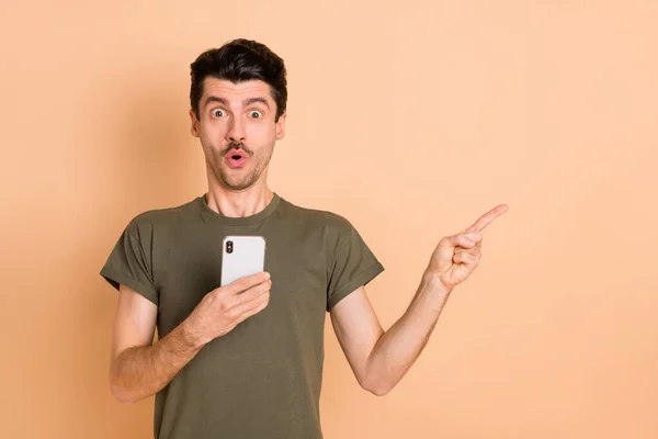 Retrato fotográfico del hombre con el dedo del smartphone apuntando espacio vacío asombrado mirando aislado sobre fondo de color beige pastel —  Fotos de Stock