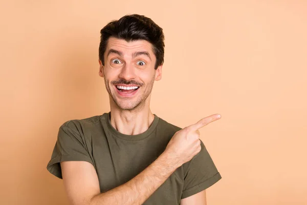 Fotoporträt von Mann lächelnd zeigt mit dem Finger auf leeren Raum überglücklich isoliert auf pastellbeige Hintergrund — Stockfoto