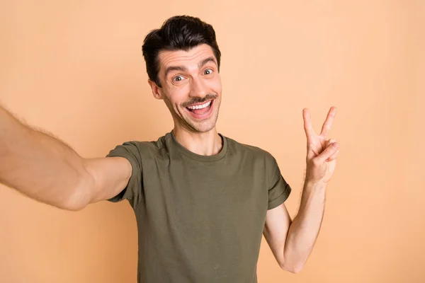 Pozitif adamın selfie çekimi, V-işareti, kamera, yeşil tişört, izole edilmiş bej arka plan. — Stok fotoğraf