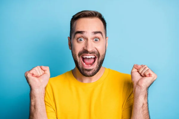 Retrato fotográfico del hombre alegre asombrado usando sudadera amarilla haciendo gestos como ganador aislado sobre fondo de color azul vivo —  Fotos de Stock