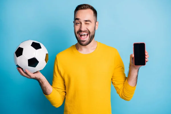 Foto portret van de mens met bal glimlachen tonen touchscreen van mobiele telefoon knipperen geïsoleerd op levendige blauwe kleur achtergrond — Stockfoto