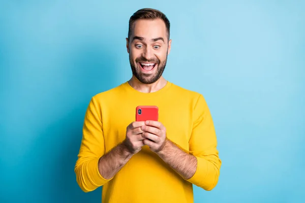 Photo portrait of amazed man wearing yellow outfit reading news smartphone staring smiling isolated on bright blue color background — 图库照片