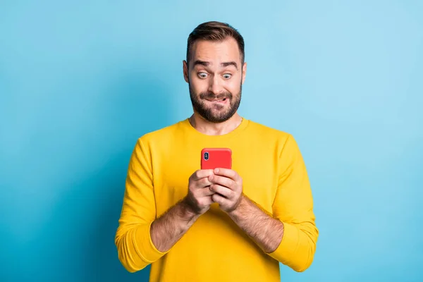 Photo of young handsome shocked amazed surprised man see unexpected news in phone isolated on blue color background — 图库照片