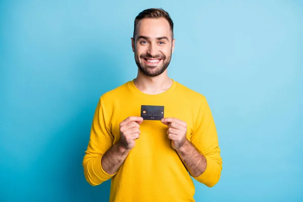 젊고 잘 생기고 긍정적 이고 기분좋은 미소를 짓고 있는 남자의 사진은 파란 배경에 고립된 신용 카드를 보여 주고 있다 — 스톡 사진