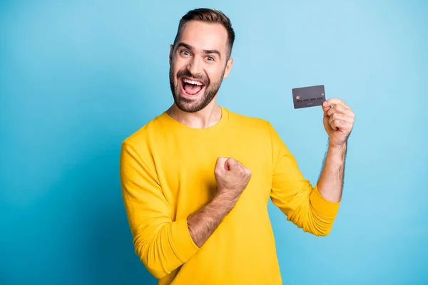 Foto van jong enthousiast blij positief vrolijk lachende man houden credit card raise vuist in de overwinning geïsoleerd op blauwe kleur achtergrond — Stockfoto