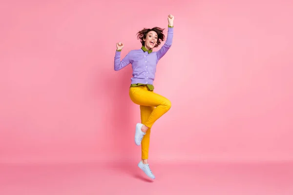 웃는 여학생 이 점프하는 사진 전체가 보라색 점퍼 노란색 바지 운동화를 단 채 핑크 색 배경을 띠고 있다 — 스톡 사진