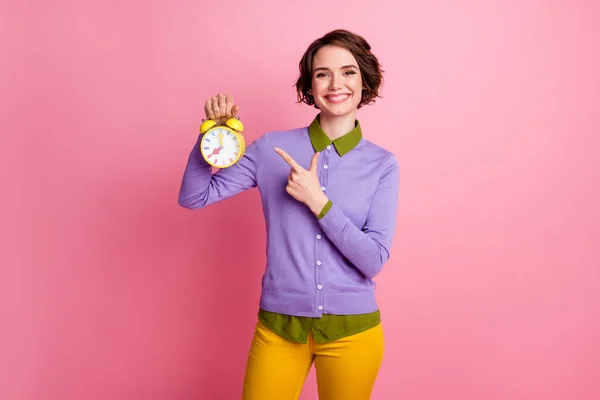 Foto van positief meisje punt index vinger klok dragen paars gele broek broek geïsoleerde pastel kleur achtergrond — Stockfoto