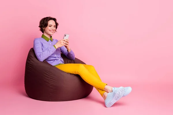 Full body profile side photo of positive girl sit bean chair use smartphone wear pants isolated pastel color background — Stock Photo, Image