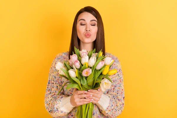 Foto van flirterig gelukkig mooi jong vrouw houd handen bloemen tulpen sturen lucht kus geïsoleerd op gele kleur achtergrond — Stockfoto