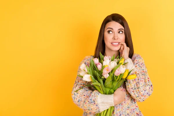 Fotografie pochybné mladé smýšlející žena kousnutí zuby nehty vzhled prázdný prostor držet květiny izolované na žlutém pozadí — Stock fotografie