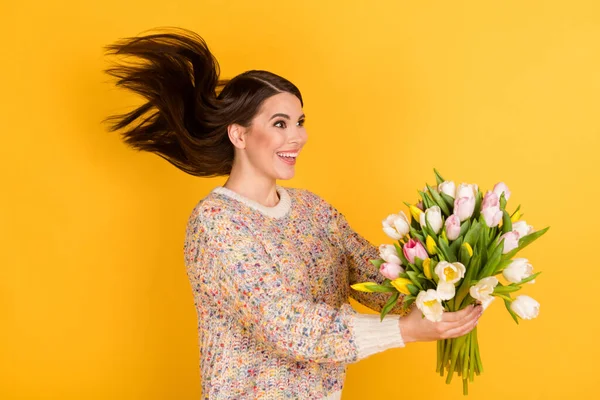 Profil sida foto av förvånad charmig ung kvinna ger blommor tomt utrymme flyga hår isolerad på gul färg bakgrund — Stockfoto